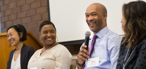 Photo of four people addressing an audience with one person holding a microphone