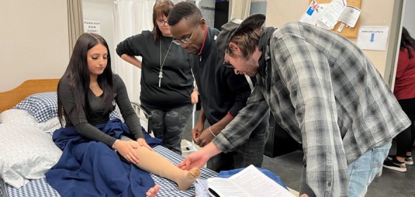 Photo of patient with leg injury being treated by three clinicians. Courtesy Kaiser Health News.