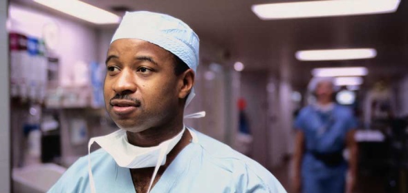  A male registered nurse in scrubs walking down a room in a hospital. 