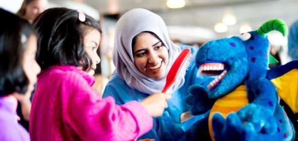 Photo of dental technician teaching two children how to brush teeth on a plushy doll