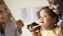 Photo of toddler using a toothbrush with mother and dentist