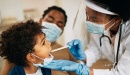 BIPOC physician providing a check up for a BIPOC child with BIPOC mother in the background. 